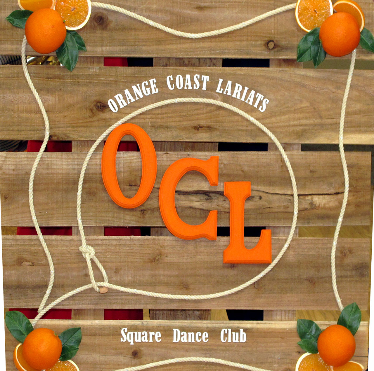 Orange Coast Lariats wooden club sign with orange OCL letters and a rope border